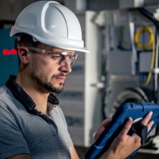 Man, an electrical technician working in a switchboard with fuses. Installation and connection of electrical equipment. Professional uses a tablet.